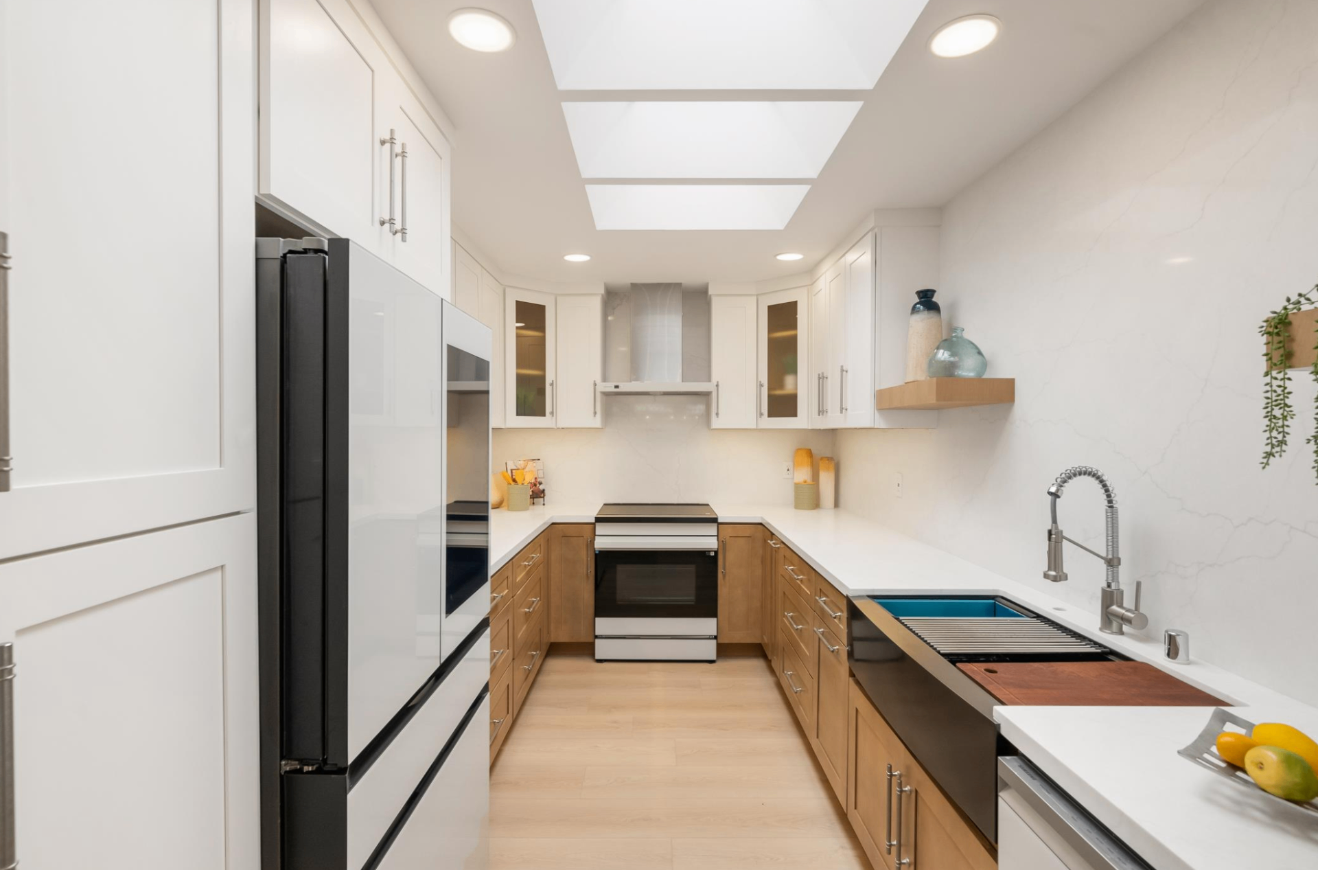 Galley kitchen with skylights, two-tone white and warm oak cabinetry, and stainless appliances