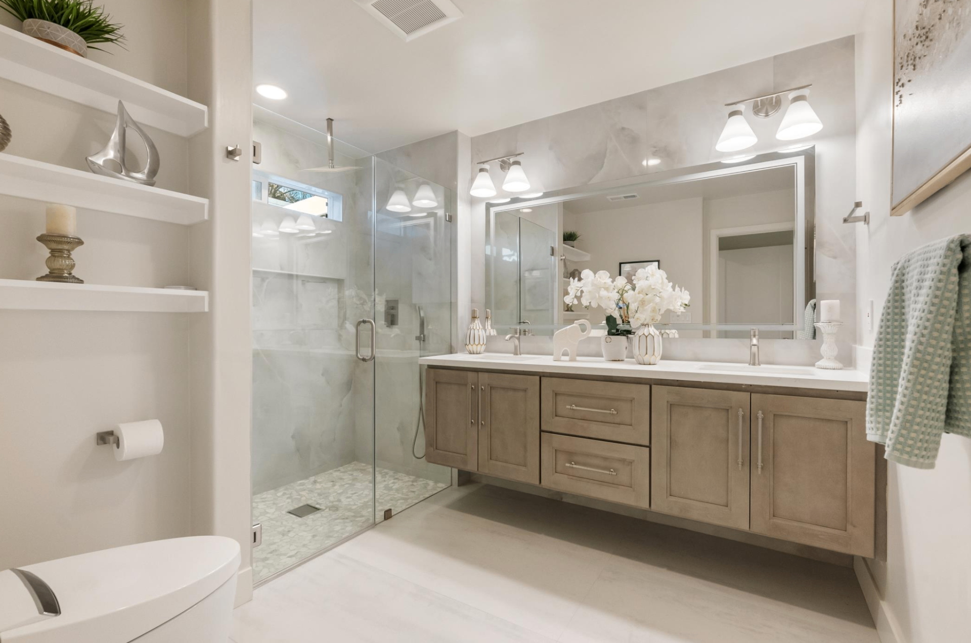 Bright bathroom with floating wood double vanity, large framed mirror, and marble walk-in shower