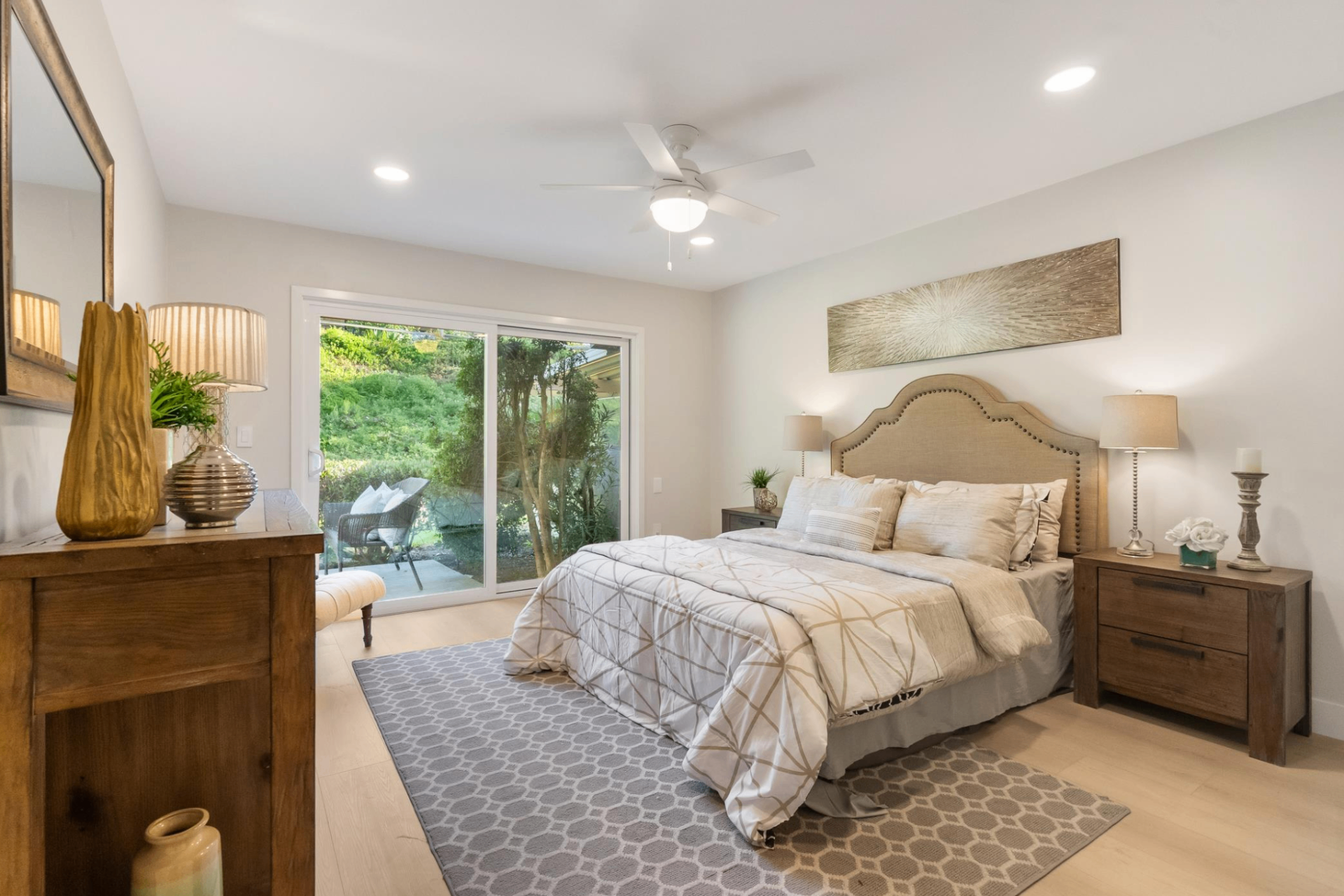 Primary bedroom with upholstered headboard, sliding glass doors to garden patio, and warm wood nightstands